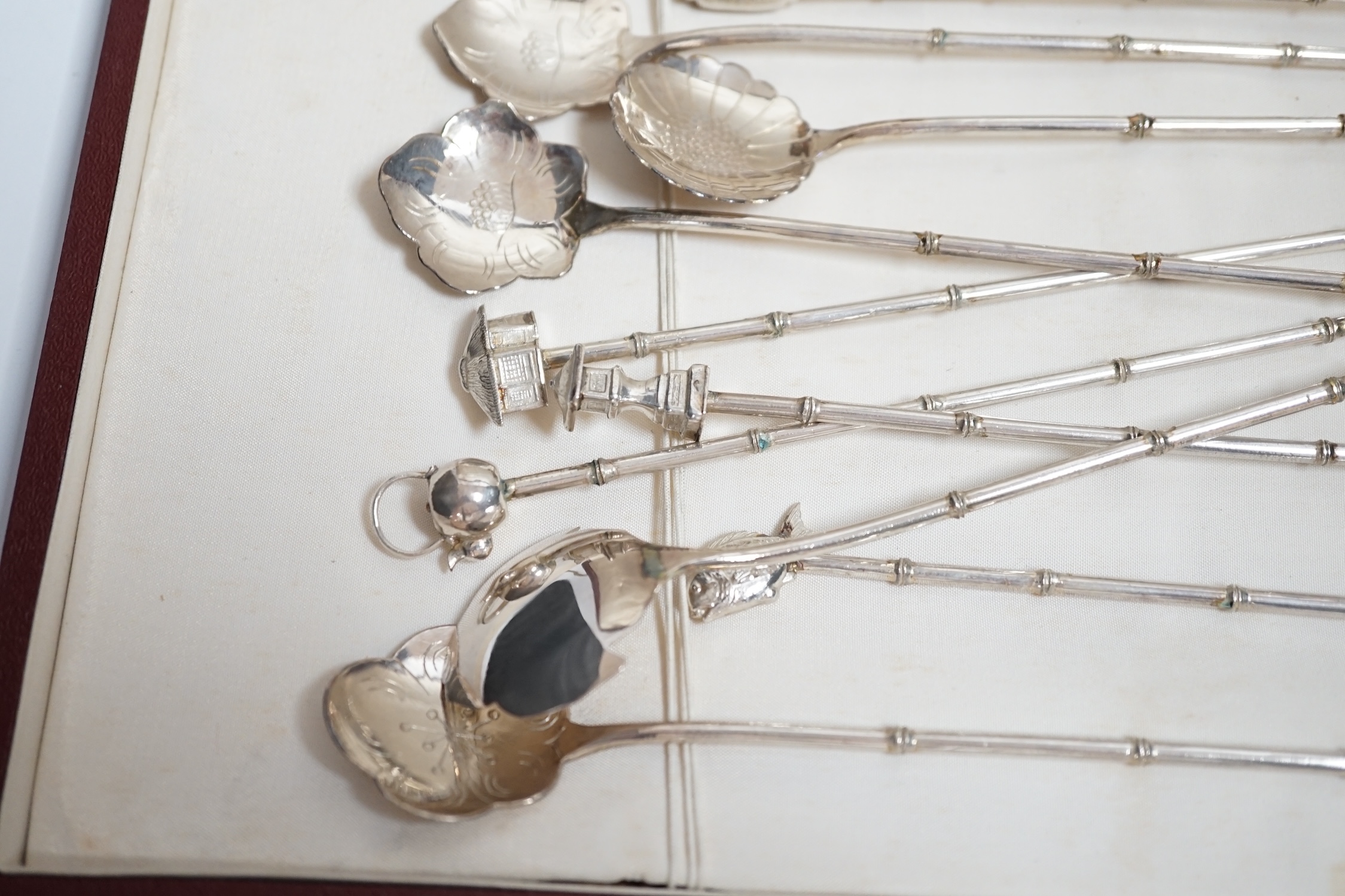 A cased set of twelve Japanese? white metal cocktail spoon, with differing terminals, 21.1cm.